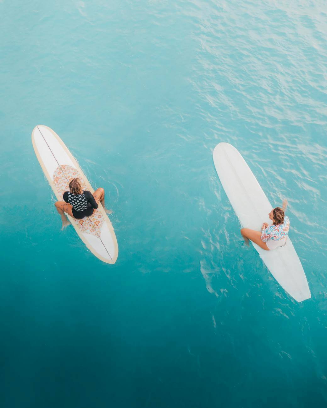 woman in white and black bikini lying on white surfboard on body of water